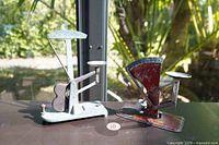 Two vintage egg scales placed side by side on a surface with natural light, showing full view and scale size comparison.