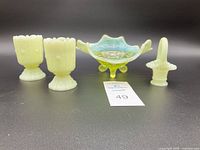 Front view of four vintage Vaseline glass pieces including footed bowl, two toothpick holders, and mini basket.