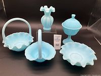 Front view of all five blue satin glass items showing two baskets, covered candy dish, ruffled bowl, and vase