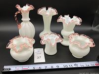 Front view of 6 vintage Fenton glass pieces including pitcher, bud vases, top hat vase, and melon bowls with rose crest detailing and a measuring tape for scale.