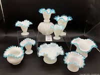 Nine vintage white opaque glass vases and bowls with aqua blue ruffled edges displayed on black background, different sizes and shapes.