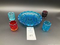 Photo showing one divided blue cut glass relish dish and four multicolored Moon & Stars pattern toothpick holders arranged around it on a black background.