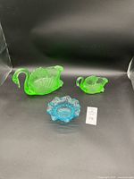 Photo of the lot showing two Vaseline glass swan figurines (one large, one small) and a blue Fenton opalescent glass bowl.