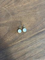 Pair of pearl stud earrings with white round pearls and gold-tone posts on a wooden surface.