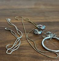 Photo showing the silver chains, decorative pendant, and hoop earrings arranged on wooden surface