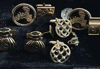 Photo showing seven vintage-style cuff links arranged on black surface. Designs include a vintage car, snowball pattern, triangular motif, and purse shape. Gold-tone metal.