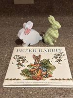 Cover of The Tale of Peter Rabbit book with two bunny figurines behind it