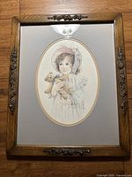 Full front view of the framed art print showing the girl with teddy bear in oval matting and wooden frame with ornate embossed metal decoration.
