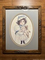Full view of framed art showing girl with doll and teddy bear in wooden frame with floral carvings.