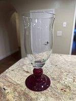 Full view of the clear glass hurricane vase with ruby base and stem, sitting on granite countertop.