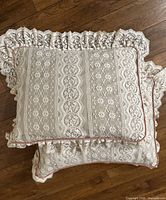 Pair of vintage white floral lace pillows with ruffled lace edges and pink piping on wood floor