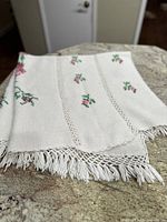Folded crochet afghan blanket showing floral embroidery and fringed edge.