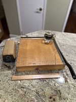Vintage Ingento wooden paper cutter with guillotine blade, metal pencil sharpener, wooden ruler, and glass paperweight displayed on granite countertop.