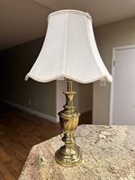 Full view of the vintage MCM brass table lamp on a countertop showing the lamp's turned brass base and cream fabric shade.