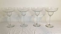 Four clear margarita glasses displayed side by side, showing full height and shape.