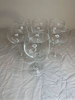 Seven clear stemmed wine glasses arranged on a soft surface to show all items included.