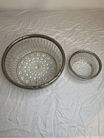 Two glass bowls of different sizes with patterned bases and metal rims placed on a white fabric background. Metal rims show rust and wear, glass appears intact.