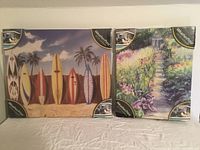 Two outdoor weatherproof prints in plastic packaging side by side on a table, showing surfboard and garden themes