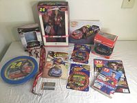 Photo showing all Jeff Gordon NASCAR memorabilia including boxed figure, toy cars, magazines, lanyard, trading cards, and collectibles arranged on a white surface.