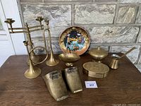 Overview of all 10 brass decor items arranged on a wooden table: stirrups, candlestick holders, covered bowl, pitcher, pate box and decorative plate
