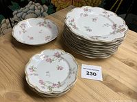 Stacked dinner and salad plates next to a salad plate and bowl on a wooden surface, showing floral pattern and gold trim