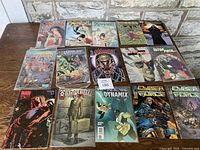 Overview of 15 comic books laid out on wood surface deck, showing front cover of each book.