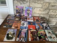 Photo showing all 17 comic books arranged on a wooden surface against a stone wall. The comics include colorful covers featuring superheroes and fantasy characters such as Daredevil and Swamp Thing.