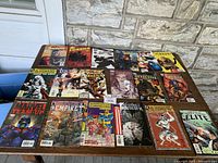 Full spread of 18 comic books arranged on table showing diverse cover art and titles.