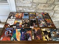 Collection of 18 vintage comic books laid out on a wooden surface in front of a stone wall. Comic titles include Emma Frost, The Punisher, Nightwing, Batman, Star Wars Republic, JLA, and others. All comics show colorful covers with various superheroes and characters.