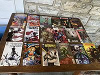 Photo showing 18 different vintage comic books arranged on wooden table with visible titles Wolverine, Superman, Gotham Central, Swamp Thing, Daredevil, Cyber Force, Maxi Mage, Queen & Country, The Out Sides, The Powers.