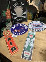 Top angled view of five vintage metal signs including Danger Beware picture frame and various gasoline and tire service advertisements.