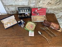 Wide shot showing all items in the lot on table including boxes, napkin rings, salt and pepper shakers, serving spoons, fork, and cranberry set.