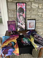 Photo showing the 7 pieces including 3 T-shirts, 2 framed posters, 2 books, displayed on a table