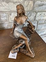 Front view of seated woman porcelain sculpture showing detailed face, hair, and draped dress on a rock-like base.