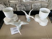 Photo showing two white Lladro cups on their stands and two Boehm flying geese figurines in front.