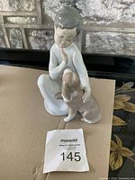 Front view of Lladro figurine boy sitting with dog on his knees.
