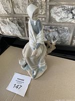 Porcelain figurine of a shepherdess girl seated wearing a bonnet and shawl, with a bird and small deer.