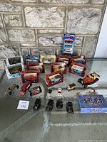 Overview of collection with multiple boxed and loose die cast cars on a glass table against a stone wall.