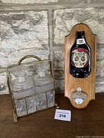 Photo showing the brass caddy with three cut glass decanters next to the wooden wall mount bottle opener with flattened glass bottle.