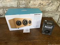 Photo showing the Sharper Image wooden Bluetooth speaker alongside the Penny Bluetooth speaker in its original box