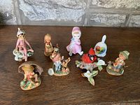 8 vintage ceramic/porcelain figurines depicting children and animals arranged on wooden surface.