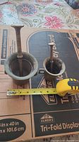 Top view comparing the sizes of the two brass mortar and pestle sets with measuring tape showing approximately 3 3/4 inches for the larger and 3 inches for the smaller.