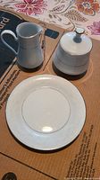 Photo of all three pieces: milk/jug creamer, lidded sugar bowl, and round plate on cardboard background.