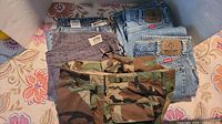 Overview of five men’s pants laid out including two Levi’s/Wrangler denim jeans, Urban Pipeline grey pants, and military camouflage pants with belt.