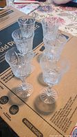 All six vintage Bohemian crystal cordial glasses arranged in loose rows on cardboard, showing clear diamond cut pattern on the bowl and stems.