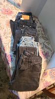 Six pairs of Calvin Klein pants and jeans laid out on a patterned bedspread showing the variety in colors and washes.