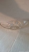 Side angle view of an oval clear glass relish dish showing starburst cut glass pattern inside and scalloped edges.