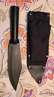 Both knives laid flat on a patterned fabric, showing the full blade and black fabric sheath with rivets and belt loops.
