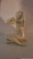 Front and side view of Gerhard Shrobek nude ceramic figurine depicting seated female figure with arms raised.