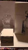 Clear crystal decanter with intricate cut design and solid stopper shown beside original box.